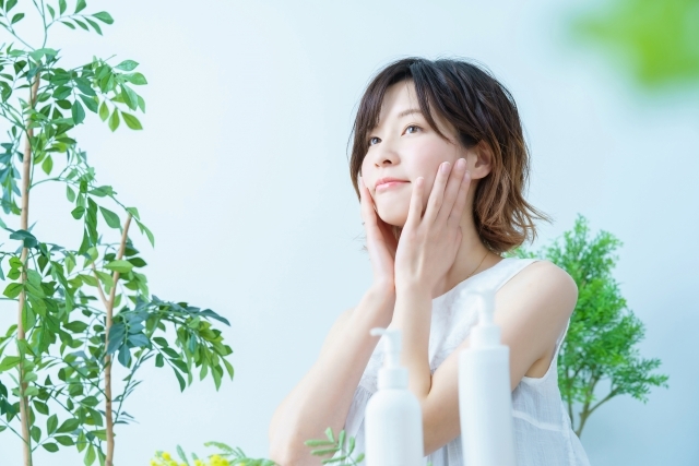 リラクゼーション･美容のイメージ画像(観葉植物の置かれた白い部屋の中で女性が化粧水をつける画像)